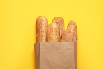 Paper bag with fresh baguettes and ciabatta on yellow background, top view