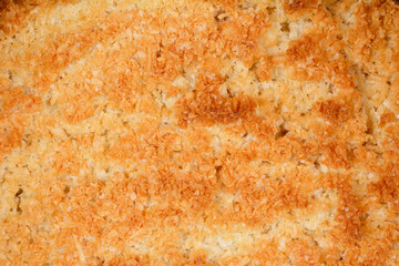 A close-up, textured view of a baked batter made from beaten egg whites and coconut, showing a golden brown, crusted surface