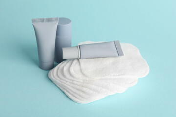 Clean cotton pads and cosmetic products on light blue background, closeup