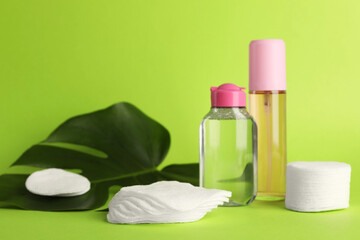 Clean cotton pads, cosmetic products and leaf on green background