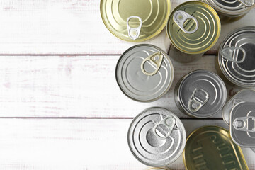 Many closed tin cans on white wooden table, flat lay. Space for text