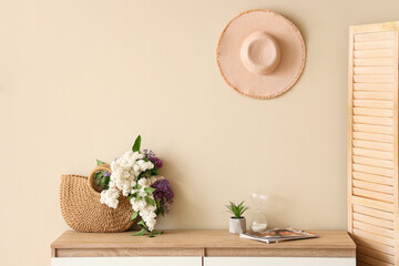 Bag with lilacs on modern chest of drawers near beige wall in room