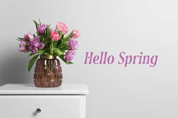 Hello Spring. Aromatic tulips in glass vase on bedside table near light wall