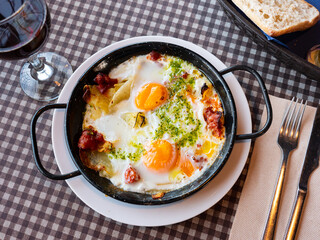 Delicious eggs a la Riojana with vegetables, bacon and chorizo sausages dressed with pesto sauce. Spanish gastronomic traditions