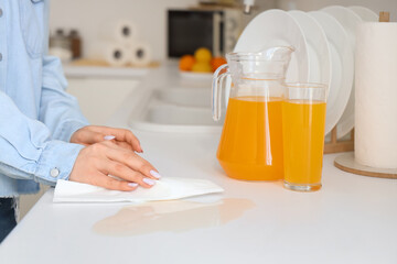 Woman wiping spilled juice with paper towel on counter in kitchen, closeup