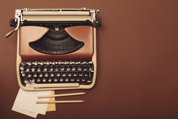 Old vintage typewriter, paper and pencils on brown background, top view. Space for text