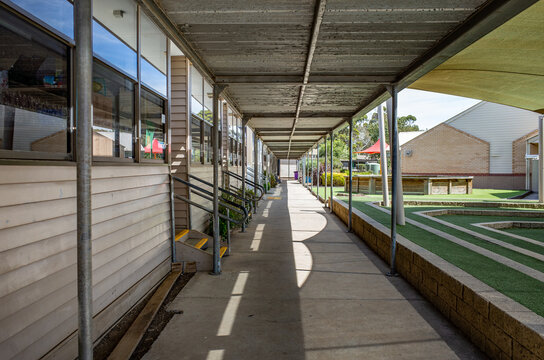 A covered concrete walkway running alongside weatherboard classroom buildings at a primary school campus in Australia. Educational facilities and outdoor space in a suburban public elementary school.