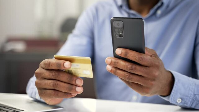 Close up of male hands using phone to make online transaction with credit card in business office. African american businessman makes digital payment, pay bills, spending money, e-commerce, e-shopping