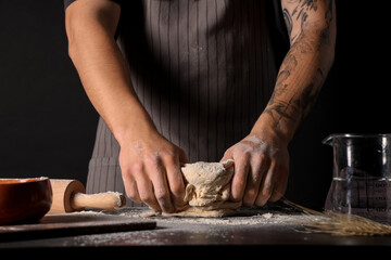 Man kneading fresh dough on table against black background