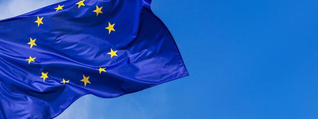 Flag of the European Union waving in the wind on flagpole against the sky with clouds on sunny day,...