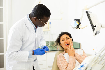 Asian woman patient talking to African American male dentist and complaining about toothache at...