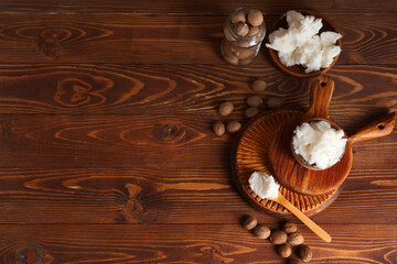 Composition with bowl of shea butter and nuts on wooden background