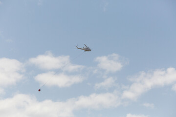 Fire fighting helicopter with trailing a water bucket on the way back to a bushfire
