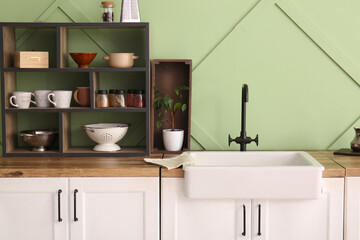 White ceramic sink and shelving unit on wooden counter near green wall in kitchen