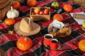 Pumpkins with cups of tea and tasty food for picnic on plaid in autumn park