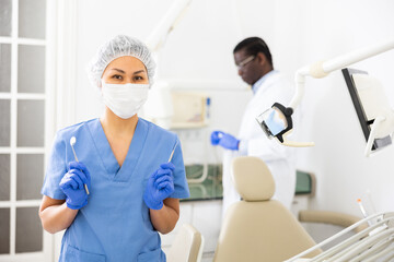 Obraz premium Portrait of a nurse with tools in her hands and wearing a medical mask in a dental office