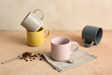 Ceramic mugs, napkin and teaspoon with coffee beans on pink table near light wall