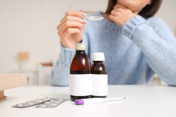 Bottles of cough syrup on table against sick woman in bedroom, closeup