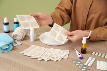 Young woman with mustard plasters and medicines at table on green background, closeup