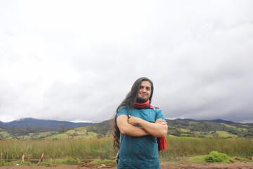 Naklejka premium A man with long hair and a beard smiles while standing in a rural area with a lake, wooden houses, and mountains in the background