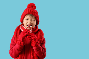 Cute fashionable boy in warm red sweater, scarf and winter hat with candy canes on blue background