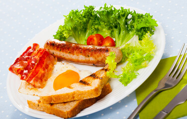 Traditional American style breakfast - fried egg with bacon, sausage and toasts garnished with fresh greens