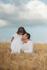 Dad and daughter hug in a wheat field.