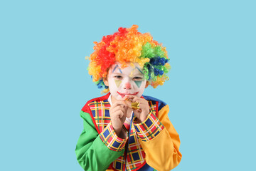 Funny little boy in clown disguise with party horn on blue background. April Fool's Day celebration