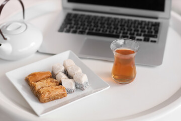 Glass of Turkish tea with sweets and laptop on table in room, closeup