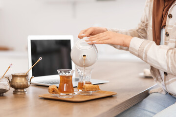 Young woman pouring Turkish tea into glass at table in kitchen, closeup