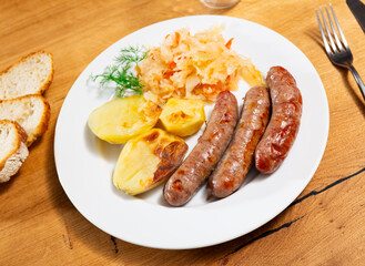 Delicious fried sausage served with potatoes and pickled cabbage on plate