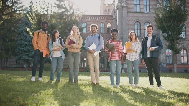 Front view of big group of people standing together outside and looking at camera while smiling. Everyone ready for upcoming classes or lectures. Professor in glasses standing in middle.