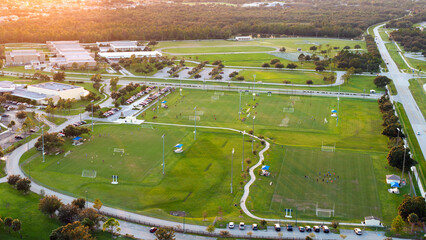 Aerial view of public sports park with children engaged in football game on grass stadium at sunset. Active way of life concept