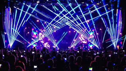 A vibrant concert scene with colorful laser lights and a cheering crowd, captured from a low-angle, reminiscent of a live music video experience.