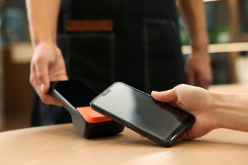 Woman paying with smartphone via terminal at wooden table in cafe, closeup