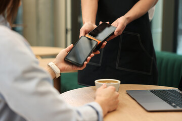 Naklejka premium Woman paying with smartphone via terminal at wooden table in cafe, closeup