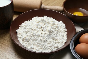 Rolling pin and ingredients for dough on wooden table, closeup