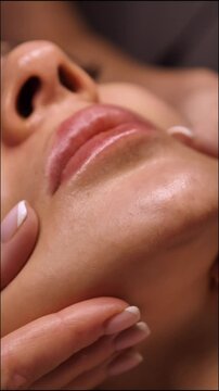 Beautician doing female anti-wrinkle rejuvenating facial massage in beauty salon, close-up, vertical