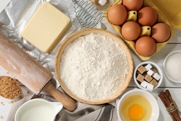 Rolling pin and ingredients for dough on white wooden table, flat lay