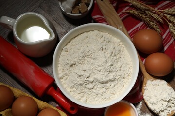 Rolling pin and ingredients for dough on wooden table, flat lay