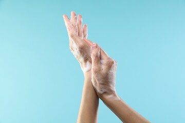 Woman washing hands with foaming soap on light blue background, closeup. Hygiene