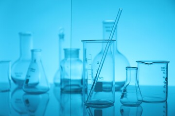 Laboratory glassware on mirror surface against light blue background