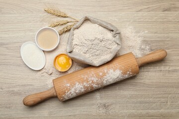 Rolling pin and different ingredients on light wooden table, flat lay