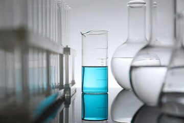 Laboratory glassware with liquid on mirror surface against light background