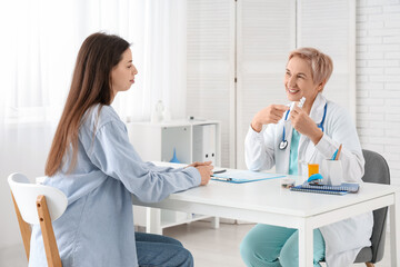 Fototapeta premium Happy mature female doctor giving pills to patient in clinic