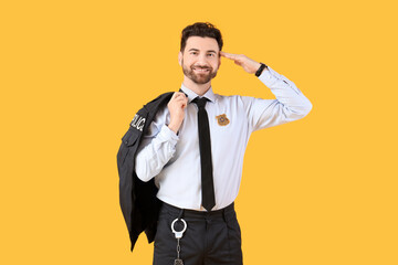 Happy male police officer with badge and handcuffs on yellow background