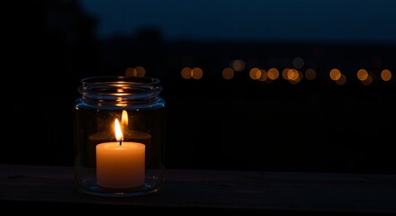 Lit candle in glass jar creating a serene and reflective atmosphere with soft bokeh lights in the background, symbolizing remembrance and peace