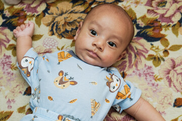 A Southeast Asian Three months old baby boy, lie down on a color mat at home, wide open eyes
