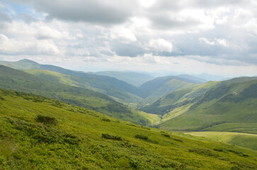 Fototapeta premium Captivating view showcasing lush green valley, surrounded by mesmerizing mountain ridges under dramatic cloudy sky, conveying sense of peace, nature's beauty, and scenic tranquility. Carpathians