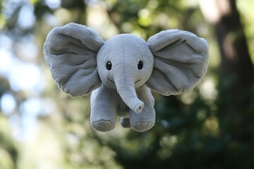Grey elephant plush toy with big ears flying outdoors in green forest background